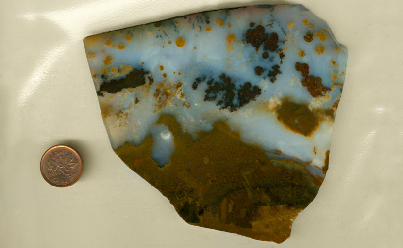 Translucent blue agate slab overlaid with black and brown spots, with a pattern of ground underneath.