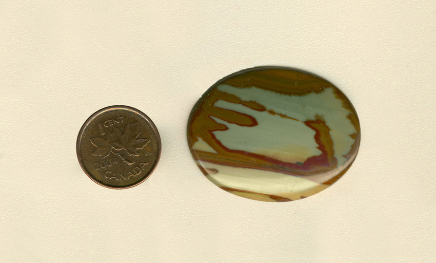 Calibrated polished Owyhee Picture Jasper cabochon from Idaho, with reddish-brown patterns on top of blue sky and yellow sand.