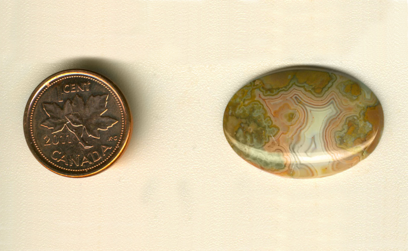 Calibrated oval polished Fairburn Agate cabochon from Nebraska or South Dakota, with orange, mint-green and blue patterning around a white fortification, on an orange background.
