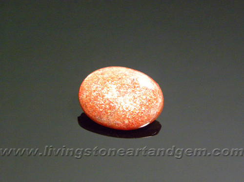 Calibrated polished Indian Sunstone cabochon, with golden-colored orange and red spangles, bright in the sunlight.