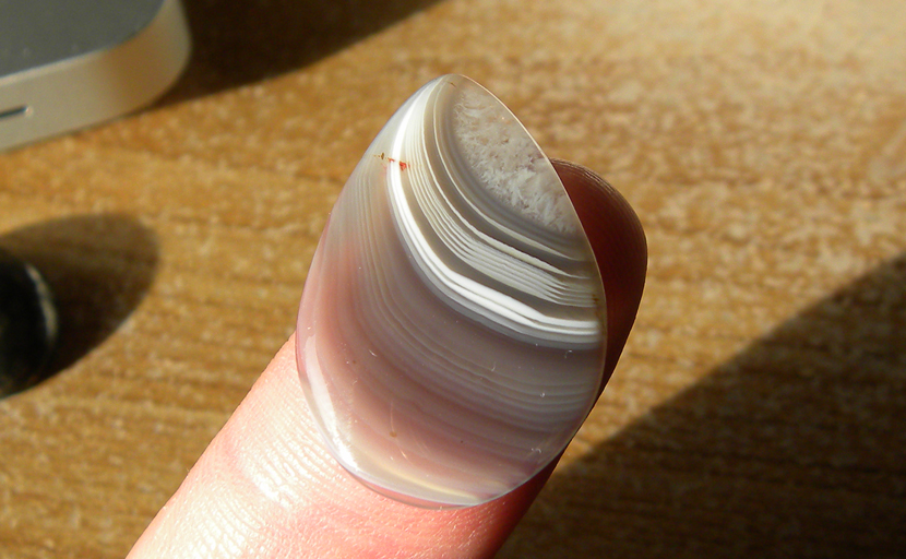 One bright red spot among white stripes on a gray background, all in a teardrop-shaped Botswana Agate cabochon.