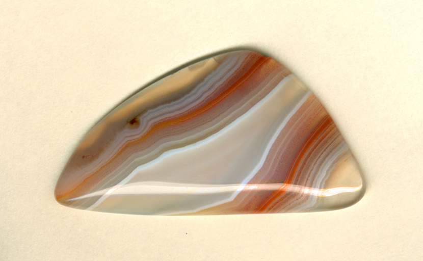 A triangular Coyamito Agate polished freeform from Mexico, translucent with overlaid stripes of pink, red and white, with accompanying dots of the same color.