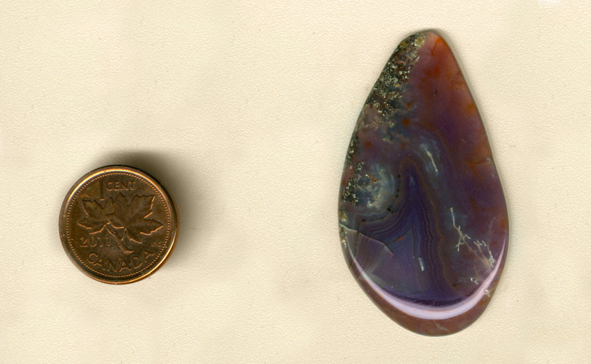 Freeform polished teardrop-shaped Parcelas Agate cabochon from Mexico, purple with fortification pattern and red and gold moss patterns.