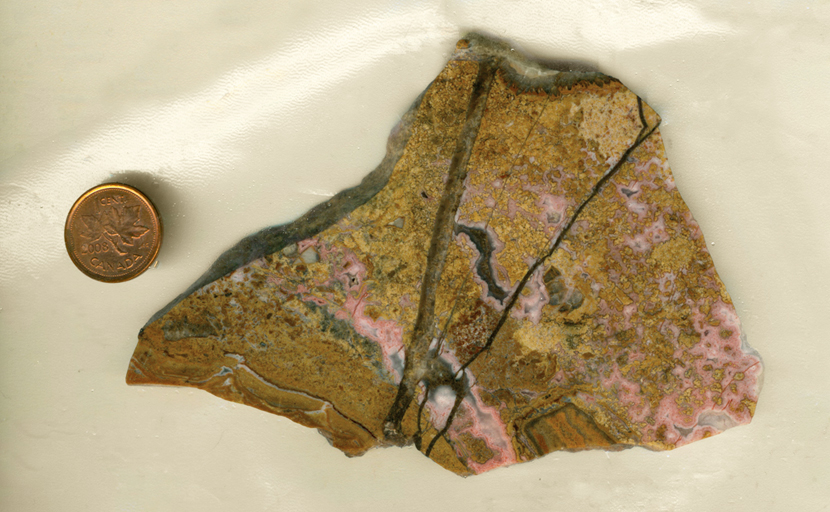 A slab of Calico Lace Agate from Mexico, with golden yellow lace patterns interspersed with pink patterns and two large black lines spreading like rays from the bottom. 