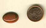 Calibrated oval polished Fairburn Agate cabochon from Nebraska or South Dakota, with a central orange double bullseye pattern on a green background, and orange concentric circles.