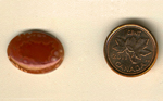 Oval polished Coyamito Agate cabochon from Mexico, red with white patterns thrusting toward the surface.