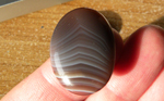 Deep purple-blue stone, with steadily receding tented white lines, in a polished cabochon of Agate from Botswana.