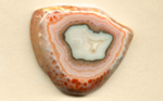 A triangular freeform Coyamito Agate from Mexico, with a white center, dark border, with a pink layer and orange spots around the outer edges.