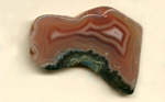 A polished, strangely shaped freeform Coyamito Agate from Mexico, orange and red with an elongated white fortification pattern in the center.