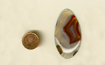 Freeform polished Laguna Agate from Mexico, with a strong red and brown fortification in colorless agate, surrounded by white fortifications and greenish spheres.