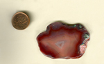 A freeform polished Laguna Agate from Mexico, colored strawberry-red, with the central fortification lightening and clearing toward the center.